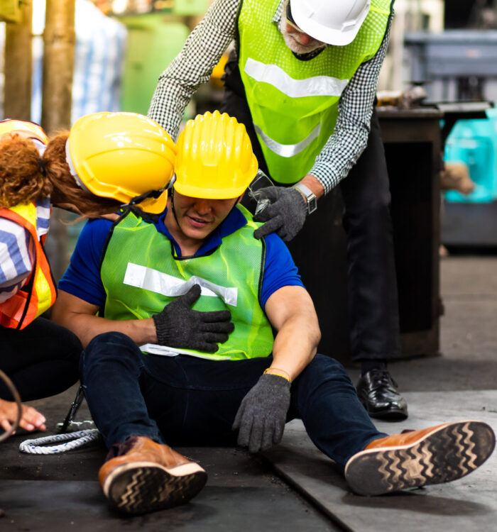 First Aid. Engineering supervisor talking on walkie talkie communication while his coworker lying unconscious at industrial factory. Professional engineering teamwork concept.